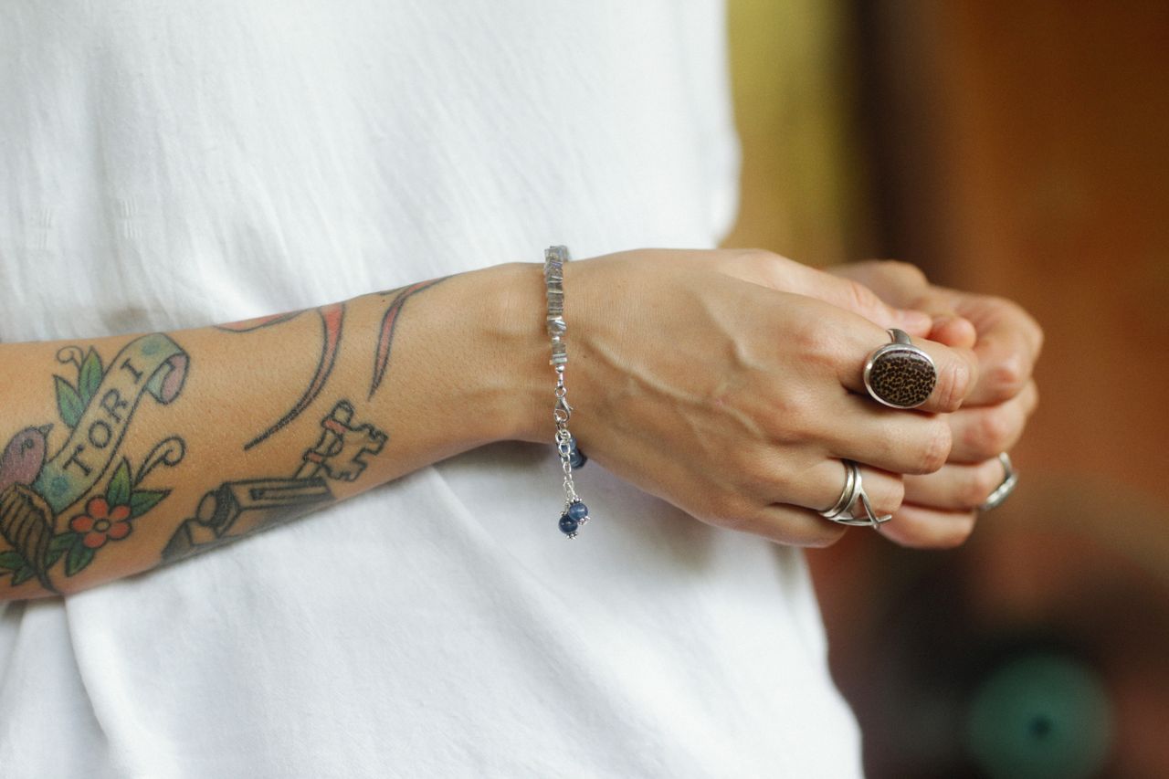 About Close-up of a tattooed arm adorned with bracelets and rings, showcasing personal style.
