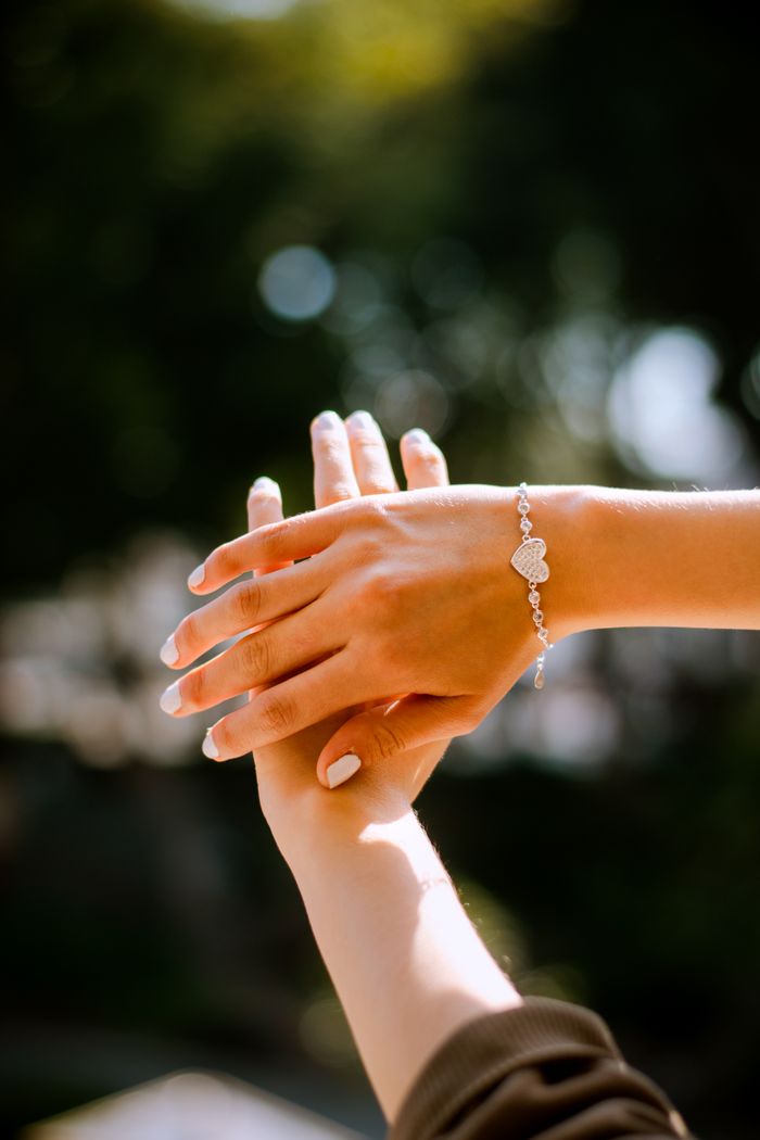 About Two hands meet in soft focus sunlight, showcasing a silver heart bracelet.